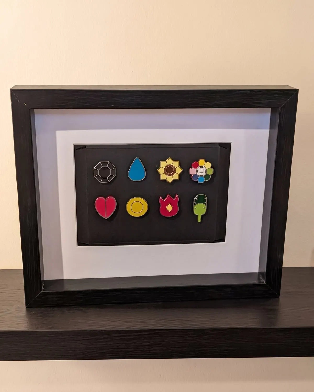 A customer's Kanto badges framed in a black shadow box on a shelf