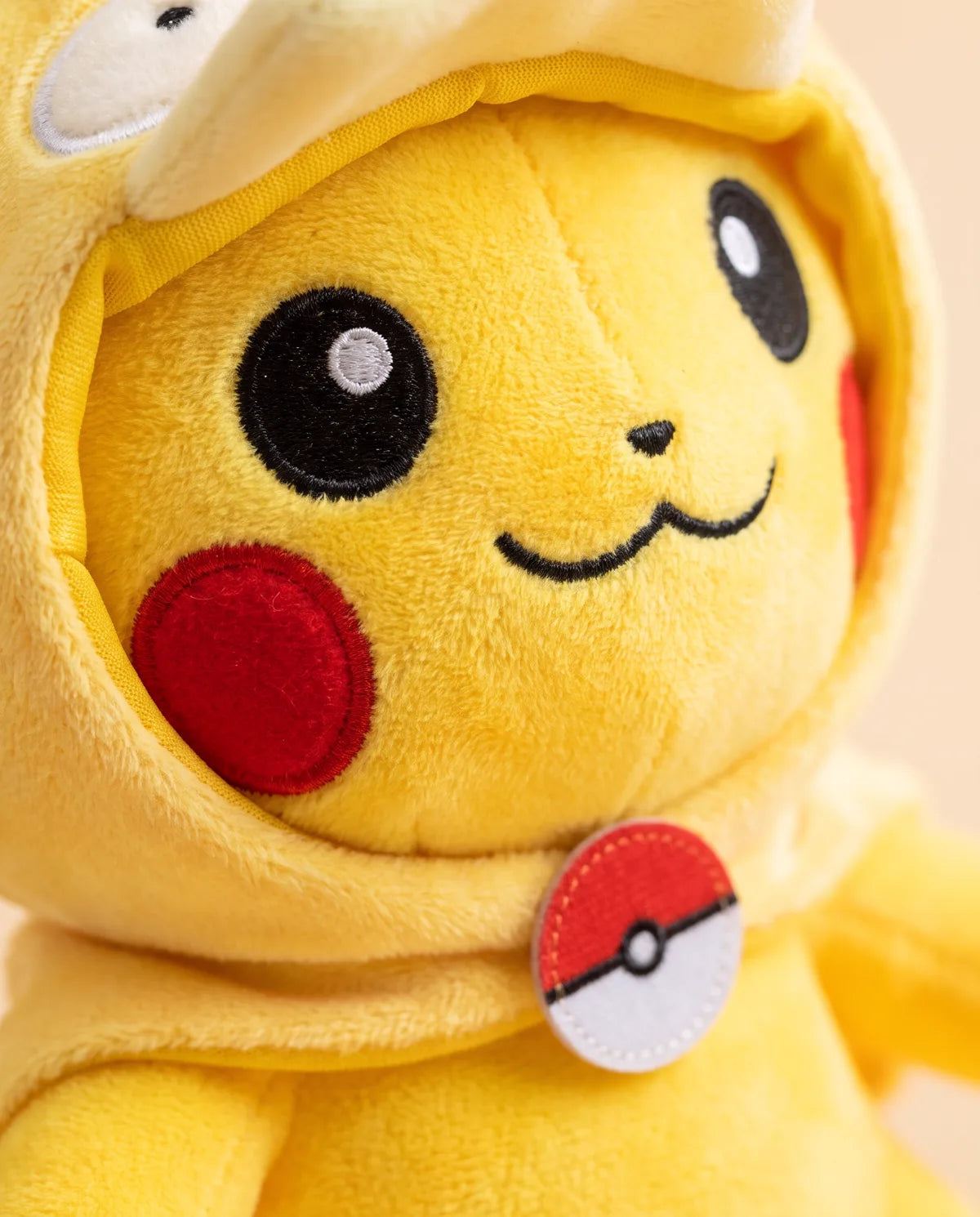 Close-up of the duck hood plush face: sewn black eyes, red cheeks, a small smile and a red-and-white ball badge at the collar