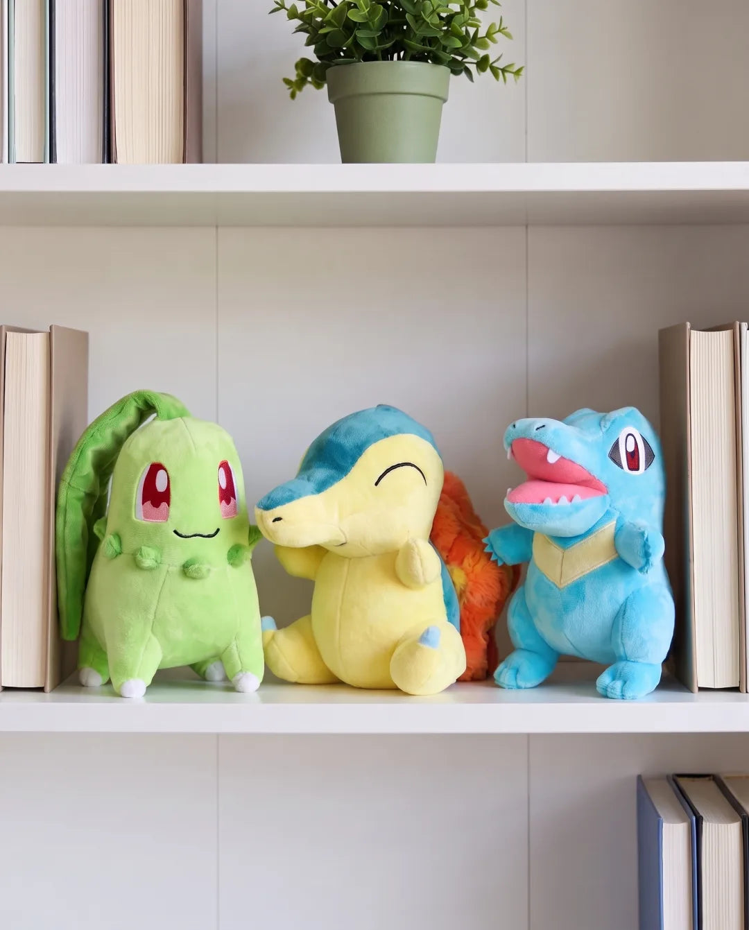 Grass #152, Fire #155 and Water #158 plush side by side on a white bookshelf between books